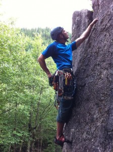 Derry climbs up a rock face with a huge rack of gear.