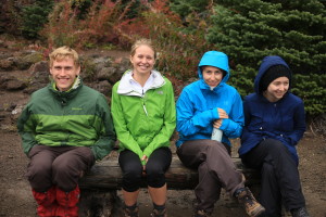 Peer pressure was only partially successful. Sitting on a bench, happy to not be in the cold water, are four hikers.
