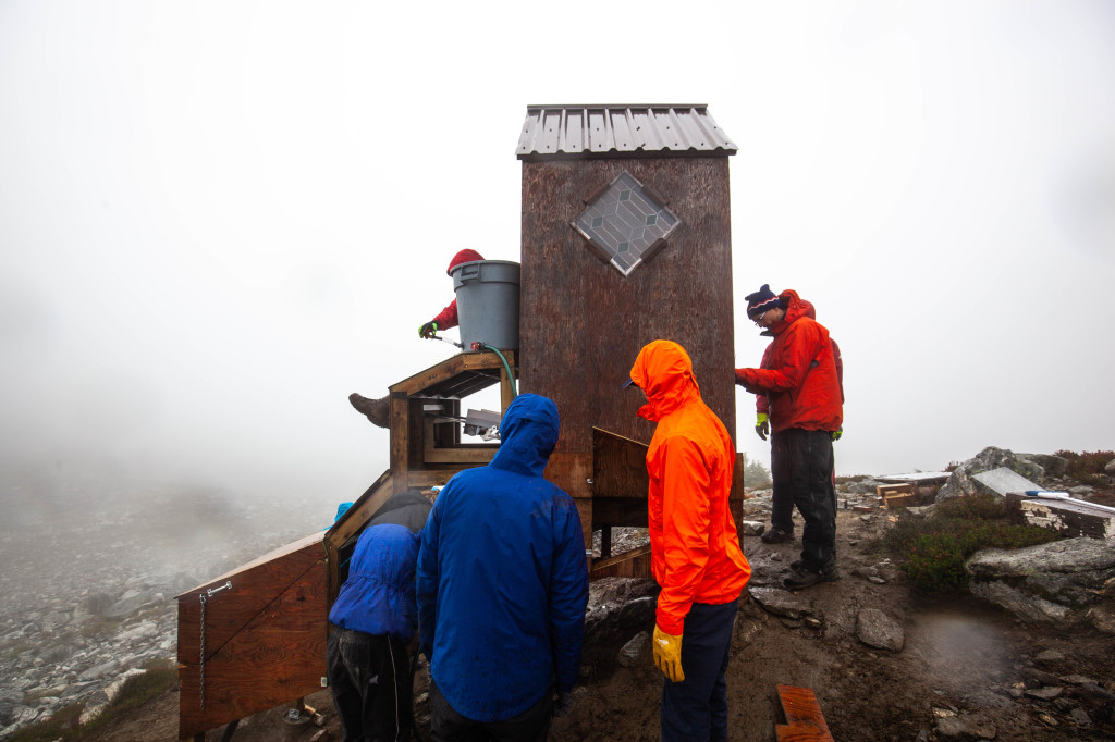 A view of the outhouse mid construction with the mechanical unit temporarily inside the structure. The top of the conveyor belt where the solid waste drops into the storage unit is visible. 