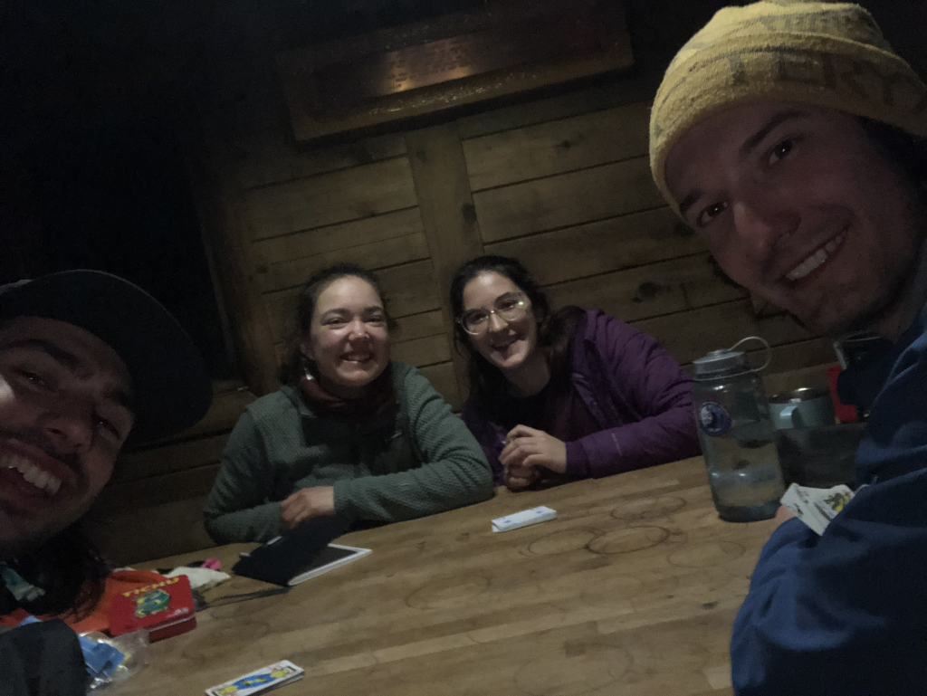 The crew having a blast eating snacks and playing cards by the woodstove.