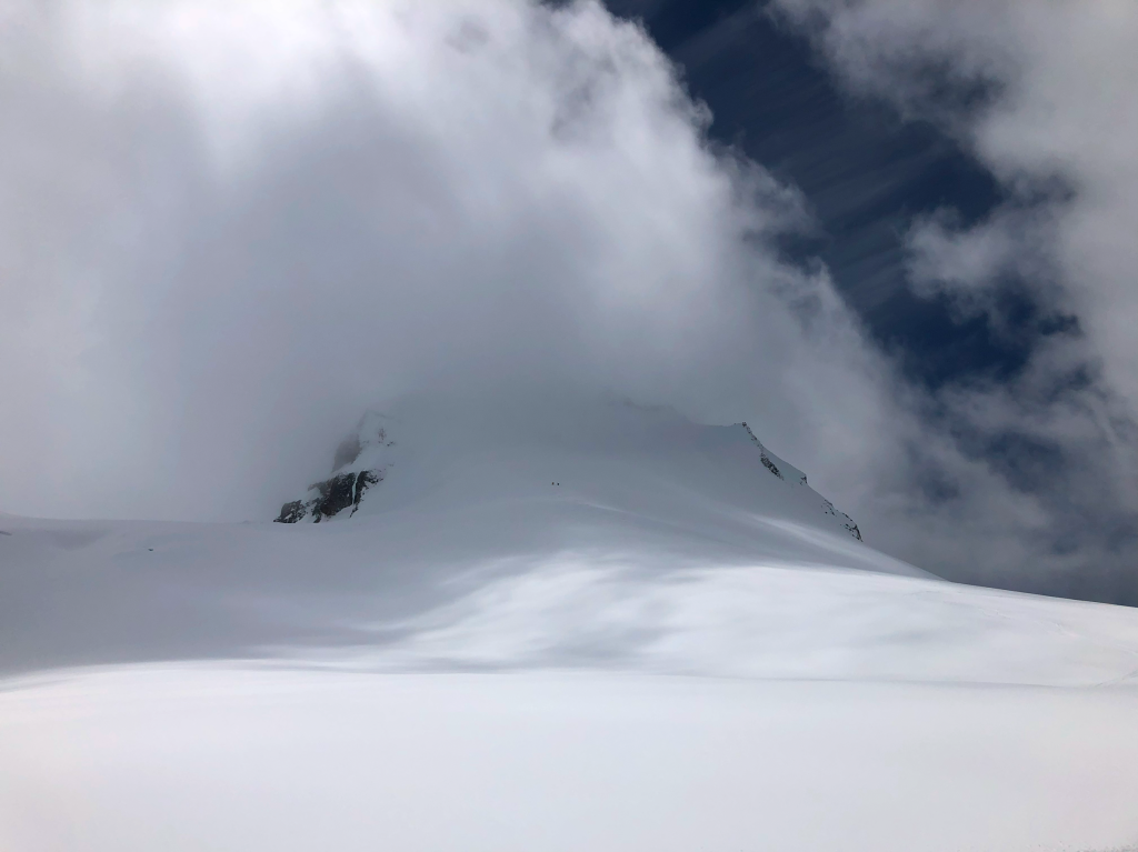 Looking back up at Nch’kay hiding away in the clouds after our ski descent. Alex and Ivan appear as two tiny dots still up on the face.